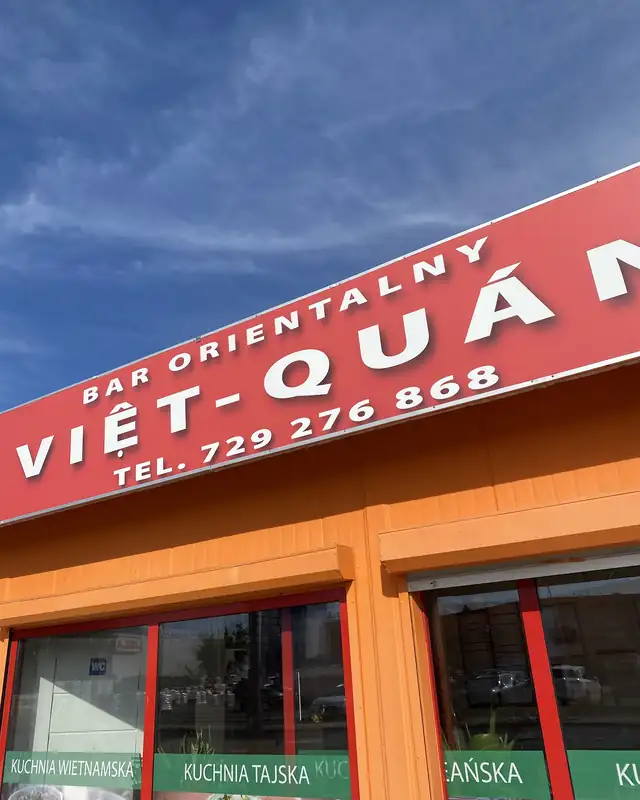 Czerwony szyld BAR ORIENTALNY VIỆT-QUÁN z numerem telefonu na pomarańczowej elewacji